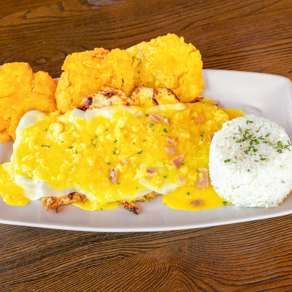 Grilled chicken topped with creamy yellow sauce, ham, white rice, and crispy tostones.