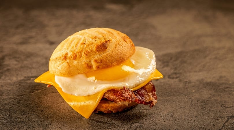 A breakfast sandwich with a fried egg, bacon, and cheese on a biscuit.