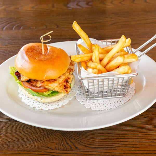 Grilled chicken sandwich with lettuce and tomato, served with a side of french fries on a white plate.