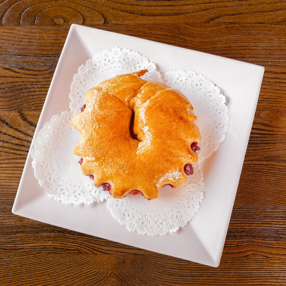 Golden ring pastry with red fruit filling on a white plate with a lace doily.
