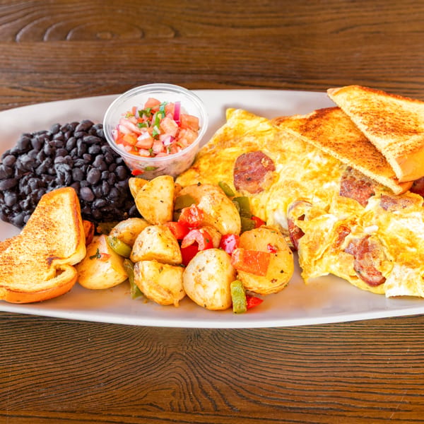 Plate of scrambled eggs with sausage, roasted potatoes, black beans, toast, and pico de gallo.