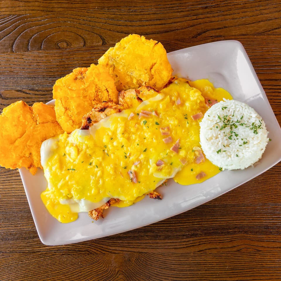 Plate with golden fried plantains, a yellow sauce dish with ham, and white rice.