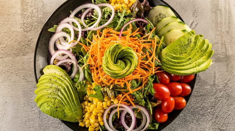 Vibrant salad with avocado, cherry tomatoes, corn, red onion, cucumber, and shredded carrots.