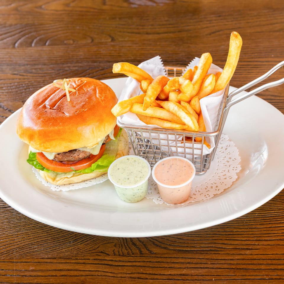 A cheeseburger with lettuce and tomato, a basket of fries, and two dipping sauces on a white plate.
