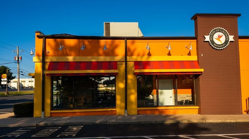 Exterior of Noches de Colombia restaurant, a vibrant orange and yellow building with red striped awnings.