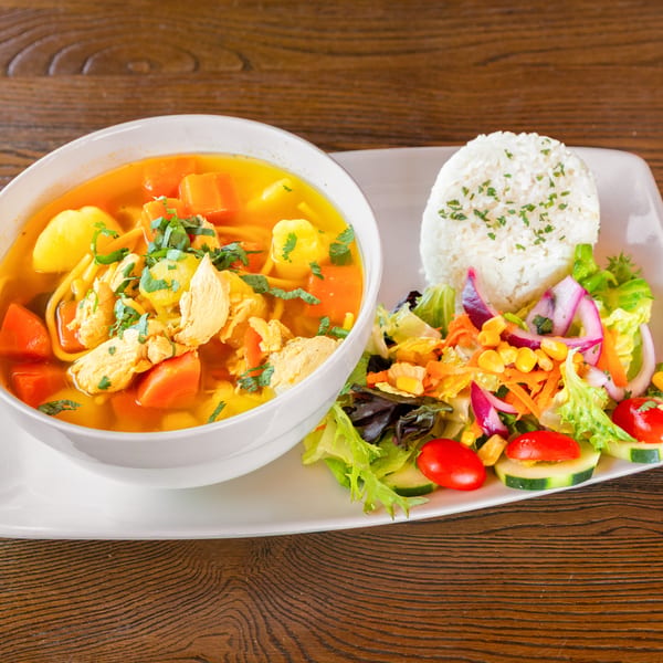 Chicken soup with carrots, potatoes, and noodles, served with white rice and a fresh side salad.