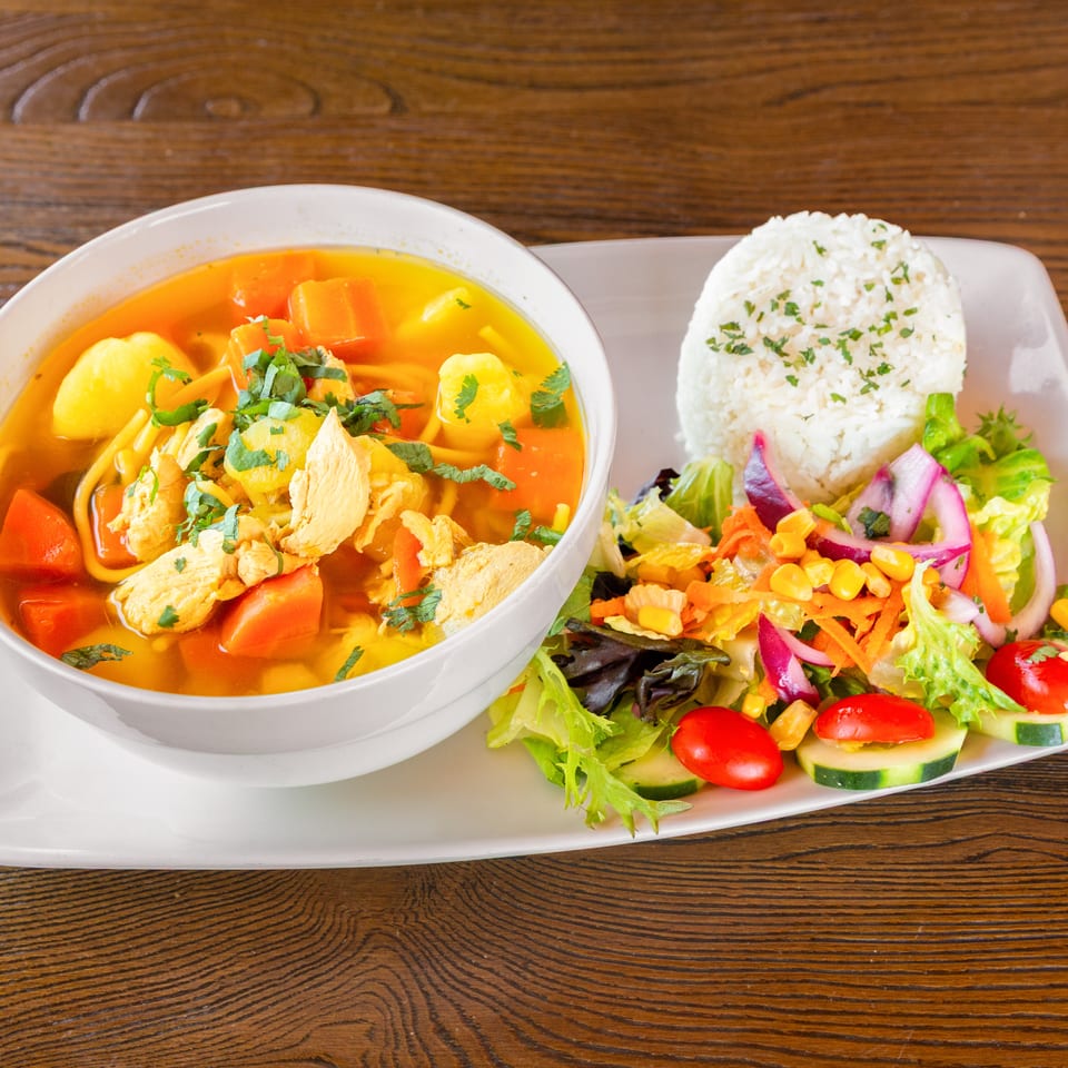 Chicken soup with carrots, potatoes, and noodles, served with white rice and a fresh side salad.