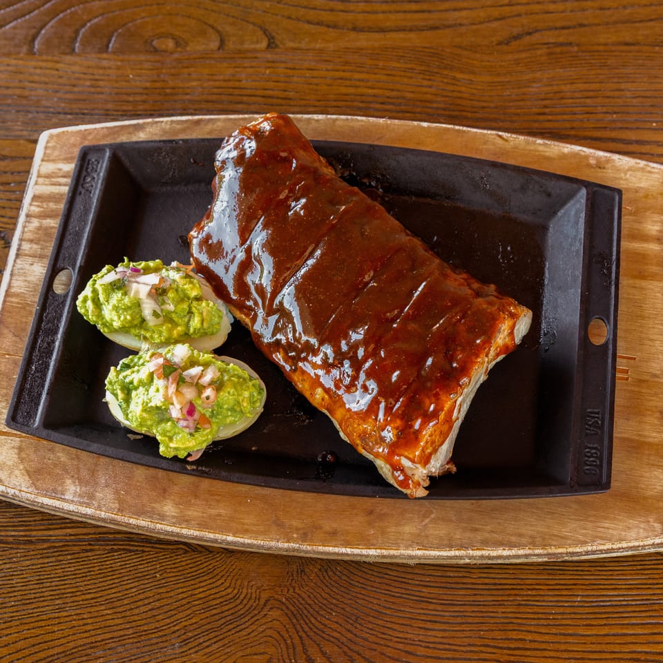 Glazed ribs and guacamole-filled potato halves on a cast iron platter and wooden board.