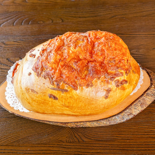 Golden-brown bread loaf with melted cheese on top, presented on a wooden board and doily.