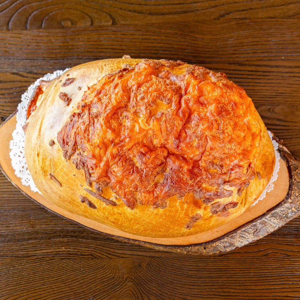 Rustic golden bread loaf with crispy melted cheese, served on a wooden board.