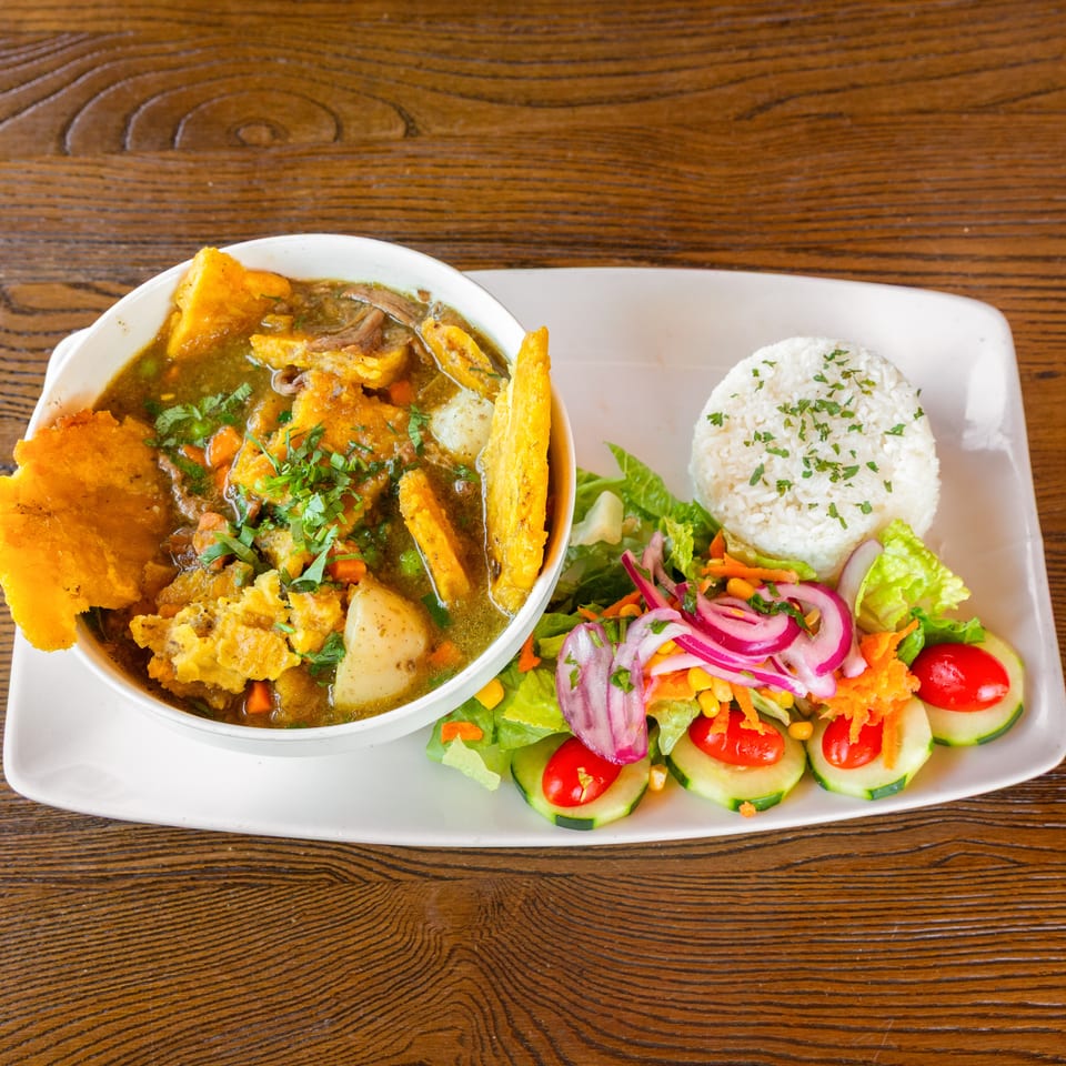 Hearty stew with plantains, white rice, and a fresh garden salad on a rectangular plate.
