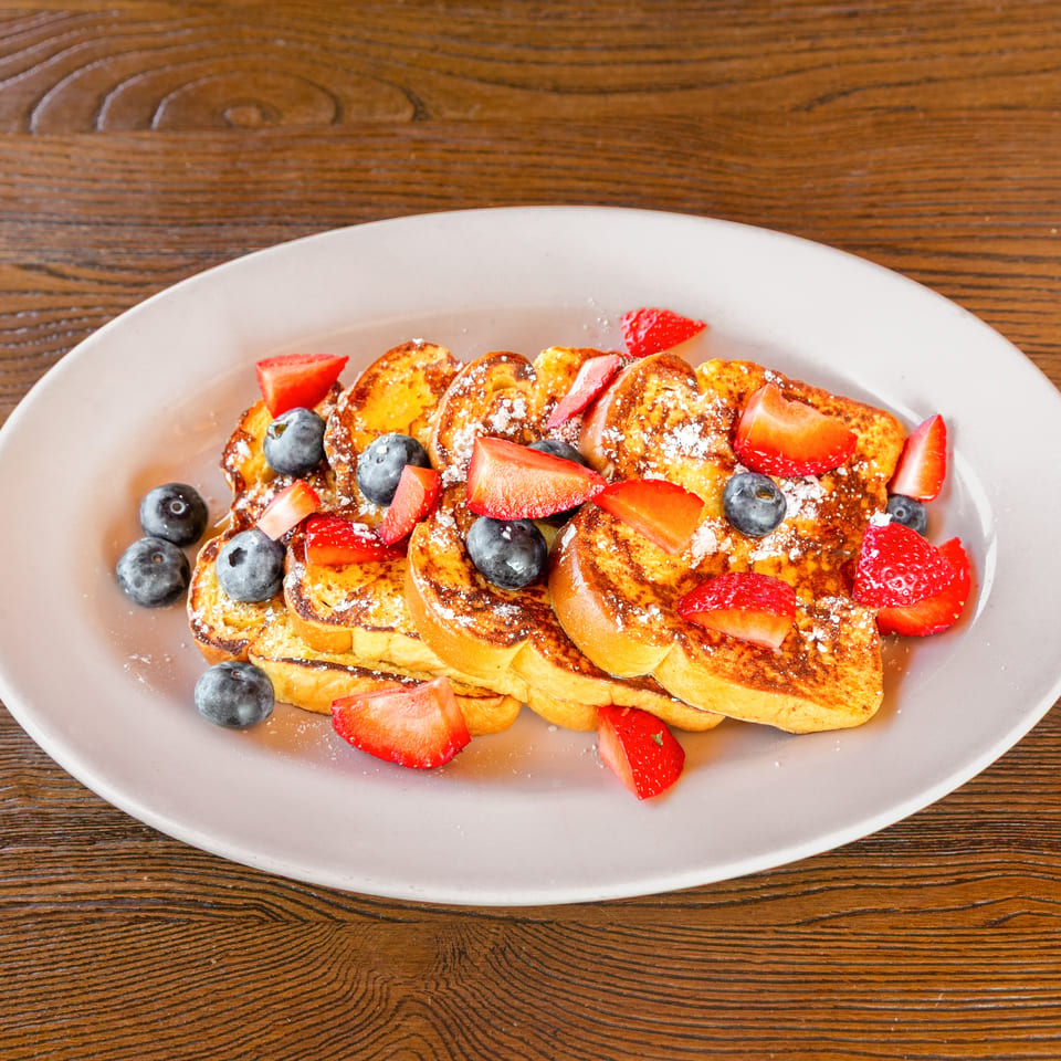 Golden French toast with strawberries, blueberries, and powdered sugar on a light plate.